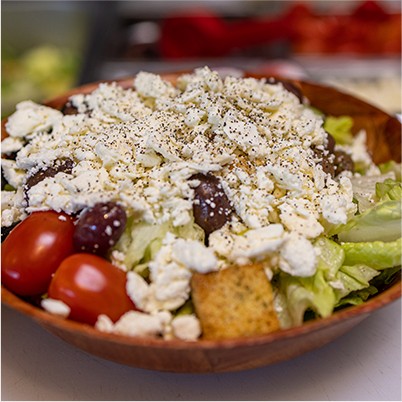 large salad in a wood bowl with cheese, tomatoes, and olives