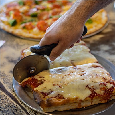 man using a cutter wheel to slice pizza